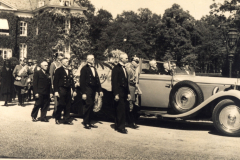 Historische Versammlung vor einem eleganten Automobil in ruhiger, parkähnlicher Umgebung