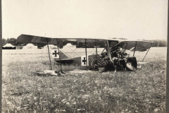 Verunglücktes Flugzeug des Ersten Weltkriegs auf einem Feld, umgeben von Zeltlagern und Graslandschaft