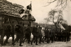 Soldaten des Ersten Weltkriegs marschieren in einer verschneiten Landschaft entlang einer Dorfstraße