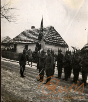 Soldaten im Ersten Weltkrieg mit Flagge vor einem traditionellen Bauernhaus in einer winterlichen Landschaft