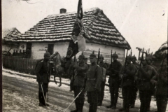 Soldaten im Ersten Weltkrieg mit Flagge vor einem traditionellen Bauernhaus in einer winterlichen Landschaft
