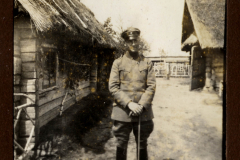 Soldat im Ersten Weltkrieg steht vor einer Gruppe von Holz- und Strohhäusern in ländlicher Umgebung