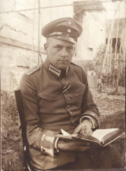 Ein Heerangehöriger sitzt im Freien und liest in einem Buch, umgeben von Pflanzen und historischem Hintergrund