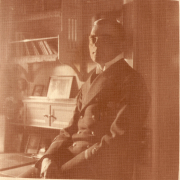 Porträt eines Offiziers in Uniform in einem gut beleuchteten Raum mit Bücherregalen und alten Fotos
