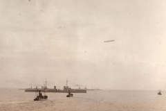 Historisches Heer im Wasser mit Schleppern und einem Luftschiff über dem Hafen