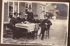 Gruppensitzung von sechs Männern in Uniform bei einem Tisch im Freien in der historischen Umgebung