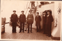 Sechs Männer der Marine stehen auf dem Deck eines Schiffs in historischer Kleidung