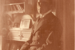 Porträt eines Offiziers in Uniform in einem gut beleuchteten Raum mit Bücherregalen und alten Fotos