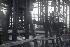 Die Aufnahme zeigt das Innere einer Werft oder Fabrikhalle mit komplexer Stahlkonstruktion und verschiedenen Maschinenbauteilen. Durch die großen Fenster der Hallenkonstruktion fällt Tageslicht auf die industriellen Anlagen und Werkstücke.