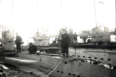 Mehrere deutsche U-Boote liegen nebeneinander in einem Hafen, wobei Besatzungsmitglieder auf den Decks und Türmen zu sehen sind. Die Aufnahme zeigt die charakteristischen Rümpfe und Aufbauten der Unterseeboote der Kaiserlichen Marine.
