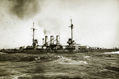 Ein deutsches Schlachtschiff der Helgoland-Klasse fährt bei bewegter See unter Dampf. Das Kriegsschiff zeigt die charakteristische Silhouette mit vier Schornsteinen und schwerer Artillerie-Bewaffnung.