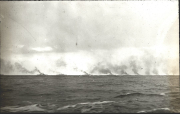 Mehrere Kriegsschiffe der Kaiserlichen Marine fahren in Formation am Horizont und erzeugen charakteristische Rauchsäulen. Die Aufnahme zeigt die Schiffe bei mäßigem Seegang aus der Distanz.