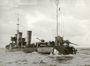 Ein deutsches U-Boot liegt längsseits eines Torpedobootes mit zwei charakteristischen Schornsteinen auf See. Auf beiden Schiffen sind Besatzungsmitglieder zu erkennen, die vermutlich einen Austausch von Material oder Personal durchführen.