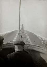 Die Aufnahme zeigt den Blick vom Kommandoturm eines U-Bootes auf das Vorderdeck mit deutlich erkennbaren Deckplanken und Ausrüstungsgegenständen. Im Hintergrund ist eine bergige Küstenlandschaft zu sehen, während im Vordergrund der Kopf eines Besatzungsmitglieds mit Mütze sichtbar ist.