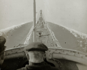 Die Aufnahme zeigt das Vorderdeck eines deutschen U-Bootes vom Turm aus fotografiert, während das Boot in schwerer See fährt. Wasser spritzt über das Deck und die Bugpartie, während das U-Boot durch die Wellen pflügt.