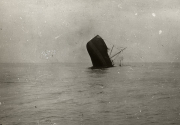 Ein Segelschiff sinkt mit dem Heck voran, während der Bug steil aus dem Wasser ragt. Die Masten und Takelage sind noch deutlich sichtbar, bevor das Schiff vollständig untergeht.