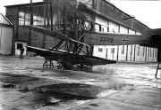 Ein deutsches Seeflugzeug mit der Kennung 2073 und Balkenkreuz steht vor einem großen Werftgebäude. Die Aufnahme zeigt das Flugzeug auf einem nassen Werftgelände mit Industriegebäuden im Hintergrund.