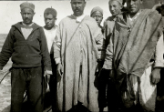 Ein deutscher Matrose in Marineuniform steht zusammen mit sechs nordafrikanischen Männern in traditioneller Kleidung. Die Aufnahme entstand vermutlich im Mittelmeerraum während einer Landoperation oder eines Hafenaufenthalts.