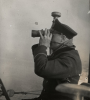 Ein Offizier der Kaiserlichen Marine benutzt ein Fernglas zur Beobachtung auf dem Turm eines U-Bootes. Er trägt eine Schirmmütze und warme Kleidung bei der Seefahrt.