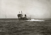 Ein Dampfschiff mit deutlicher Schlagseite und starker Rauchentwicklung sinkt auf bewegter See. Das Schiff zeigt bereits eine kritische Neigung, während Gischt und Wellen um den Rumpf schlagen.