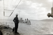 Ein Marineoffizier beobachtet von Deck eines U-Bootes aus ein anderes deutsches U-Boot in geringer Entfernung auf See. Im Hintergrund sind Berge oder Küstenlinien erkennbar, was auf Operationen im Mittelmeerraum hindeutet.
