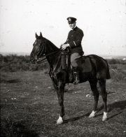 Ein Offizier der Kaiserlichen Marine in dunkler Uniform und Schirmmütze sitzt auf einem dunklen Pferd in einer offenen Landschaft. Die Aufnahme zeigt eine Reitszene abseits des maritimen Dienstes, möglicherweise während eines Landaufenthalts oder Ausflugs.