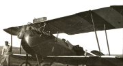 Ein deutsches Militärflugzeug steht auf einem Flugfeld, während Besatzungsmitglieder in der Nähe des Flugzeugs positioniert sind. Das Flugzeug zeigt die typische Bauweise der Kaiserlichen Luftstreitkräfte mit Doppeldecker-Konstruktion und Propellerantrieb.