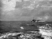 Ein deutsches Kriegsschiff der Kaiserlichen Marine fährt bei stürmischen Wetterbedingungen und hohem Seegang. Das Schiff ist in der Ferne zu erkennen, während im Vordergrund die aufgewühlte See mit schäumenden Wellenkämmen zu sehen ist.