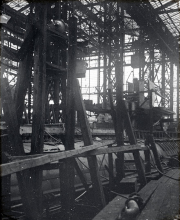 Die Aufnahme zeigt das Innere einer Werft oder Fabrikhalle mit komplexer Stahlkonstruktion und verschiedenen Maschinenbauteilen. Durch die großen Fenster der Hallenkonstruktion fällt Tageslicht auf die industriellen Anlagen und Werkstücke.