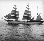 Ein großes Segelschulschiff mit drei Masten und vollständig gesetzten Segeln fährt bei ruhiger See. Das Schiff zeigt die charakteristische Takelung eines Vollschiffs mit quadratischen Rahsegeln.