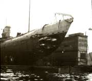 Ein deutsches U-Boot liegt zur Wartung oder Reparatur in einem Trockendock einer Marinewerft. Die Aufnahme zeigt das Unterseeboot von der Seite mit sichtbarem Turm und Rumpf sowie den Dockanlagen.