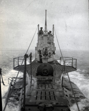 Aufnahme vom Deck eines deutschen U-Bootes während der Fahrt auf See mit Blick auf den Kommandoturm. Mehrere Besatzungsmitglieder sind auf der Brücke und am Turm zu sehen, während das Boot durch bewegte See fährt.