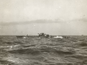 Ein deutsches U-Boot fährt aufgetaucht durch bewegte See mit sichtbarer Besatzung auf dem Turm. Am Horizont ist ein weiteres Schiff zu erkennen.