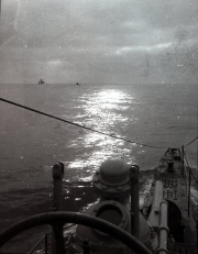 Die Aufnahme zeigt das Vorderdeck eines deutschen U-Bootes mit Turm und Deckgeschütz bei Sonnenuntergang. Am Horizont sind zwei weitere Schiffe der Kaiserlichen Marine zu erkennen.