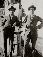 Zwei Offiziere der Kaiserlichen Marine stehen in Zivilanzügen und Hüten auf dem Deck eines U-Bootes. Im Hintergrund sind der Kommandoturm und technische Ausrüstung des Unterseebootes zu erkennen.