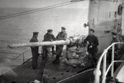 Mehrere Marinesoldaten in Uniformen handhaben einen Torpedo auf dem Deck eines U-Bootes auf See. Die Aufnahme zeigt den Vorgang der Torpedoübernahme während einer Feindfahrt im Ersten Weltkrieg.