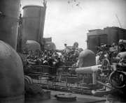 Marineangehörige der Kaiserlichen Marine musizieren mit Blasinstrumenten auf dem Deck eines Kriegsschiffes. Die Aufnahme zeigt Geschütze, Aufbauten und technische Ausrüstung des Schiffes im Hintergrund.