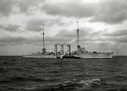 Ein deutscher Kreuzer mit drei charakteristischen Schornsteinen fährt bei bewegter See unter bewölktem Himmel. Das Kriegsschiff zeigt die typische Silhouette eines Kreuzers der Kaiserlichen Marine aus der Zeit des Ersten Weltkriegs.