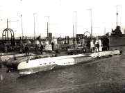 Mehrere deutsche U-Boote liegen nebeneinander in einem Marinehafen vor Anker. Besatzungsmitglieder sind auf den Decks und an den Türmen der Unterseeboote zu erkennen.