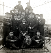 Gruppenaufnahme der Besatzung des deutschen U-Boots S.M. U 39 mit Offizieren in dunklen Uniformen und Matrosen in Marineanzügen. Die Aufnahme zeigt die Mannschaft auf dem Deck des U-Boots mit Werftanlagen im Hintergrund.