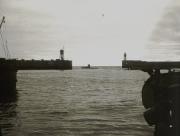 Blick durch eine Hafeneinfahrt zwischen zwei Molen mit Leuchttürmen auf ein U-Boot in der Ferne. Die Aufnahme erfolgte von Bord eines anderen Schiffes aus.