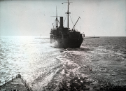 Ein deutsches Kriegsschiff mit charakteristischem Schornstein und Masten fährt auf ruhiger See. Die Aufnahme wurde vom Deck des U-Bootes S.M. U 39 aus gemacht, erkennbar am Reling im Vordergrund.