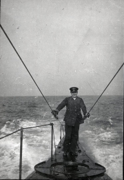 Ein Marineoffizier der Kaiserlichen Marine steht auf dem Turm eines U-Bootes bei rauer See. Das Bild zeigt die Aufbauten des Turms mit Antennendrähten und das aufgewühlte Wasser um das Fahrzeug.