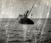 Ein Dampfschiff sinkt im Meer, wobei die Schornsteine und Masten noch aus dem Wasser ragen. Die Aufnahme dokumentiert den fortgeschrittenen Sinkvorgang eines Handelsschiffes während des Ersten Weltkriegs.