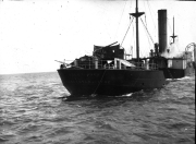 Ein Kriegsschiff mit einem Schornstein und sichtbaren Kampfschäden am Heck fährt durch bewegte See. Die Aufnahme zeigt deutliche Zerstörungen an der Heckpartie des Schiffes.