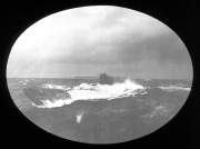 Ein deutsches U-Boot fährt bei schwerem Seegang an der Oberfläche, wobei hohe Wellen über das Deck brechen. Die Aufnahme zeigt das Fahrzeug in bewegter See mit deutlich sichtbarer Gischtbildung um den Kommandoturm.