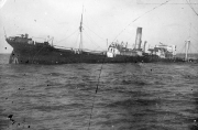 Ein großes Dampfschiff sinkt nach einem U-Boot-Angriff und liegt bereits stark auf der Seite im Wasser. Das Schiff zeigt deutliche Schlagseite und befindet sich im fortgeschrittenen Sinkvorgang.