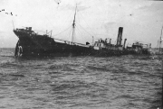 Ein großes Dampfschiff liegt schwer beschädigt und sinkend im Wasser, mit deutlich sichtbarer Schlagseite nach Steuerbord. Das Schiff zeigt typische Merkmale eines Handelsschiffes mit Masten, Aufbauten und Schornstein.