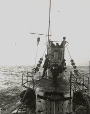 Mehrere Besatzungsmitglieder des deutschen U-Boots S.M. U 39 stehen auf und um den Kommandoturm während einer Überwasserfahrt. Das Deck und die charakteristische Turmkonstruktion mit Periskop und Sehrohr sind deutlich erkennbar.