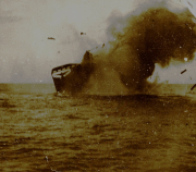 Ein Handelsschiff sinkt mit dem Heck voran ins Meer, während dichter schwarzer Rauch aus dem Schiff aufsteigt. Die Aufnahme dokumentiert eine Schiffsversenkung im Rahmen des U-Boot-Krieges der Kaiserlichen Marine.